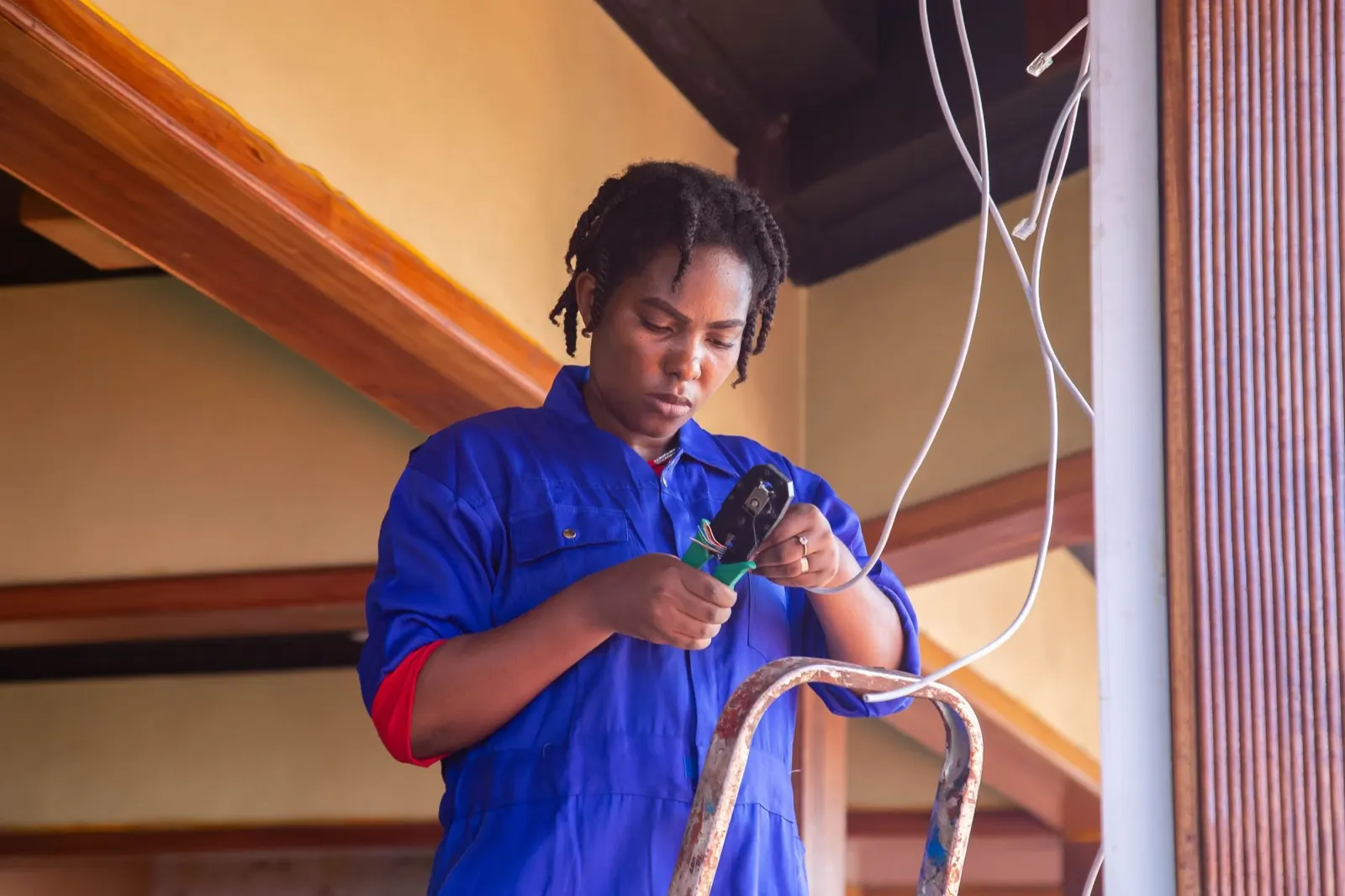 Electrician in blue coveralls stripping cable on a stepladder indoors