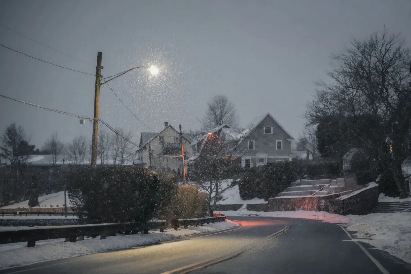 Snow falling on a quiet suburban street at dusk under a streetlight