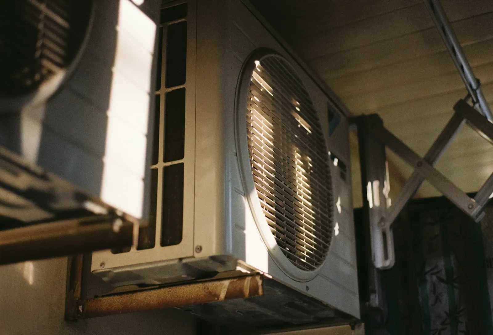 Weathered outdoor air conditioning condenser on a rusted wall bracket