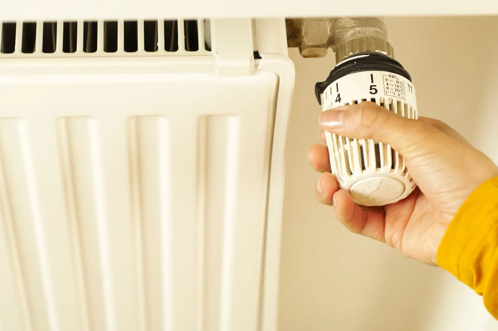 Hand turning the thermostatic valve on a white radiator