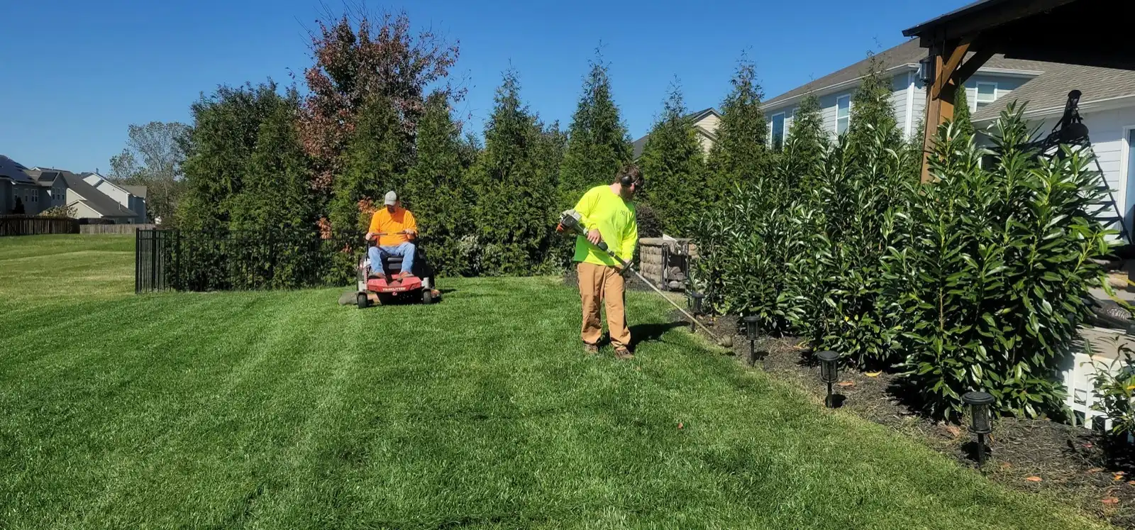 Two-person lawn crew mowing and string-trimming a striped residential lawn