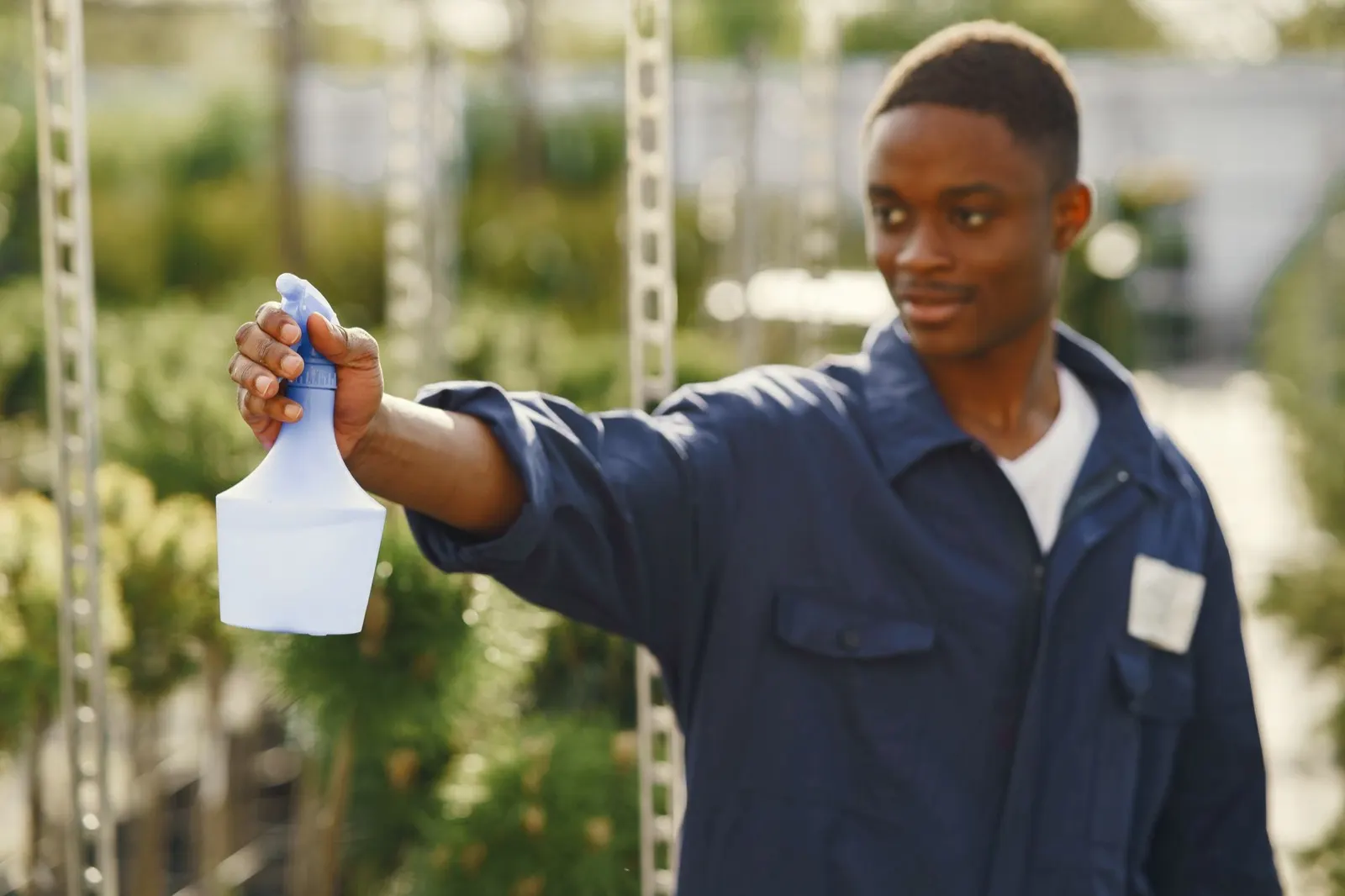 Smiling technician in navy coveralls holding a spray bottle outdoors