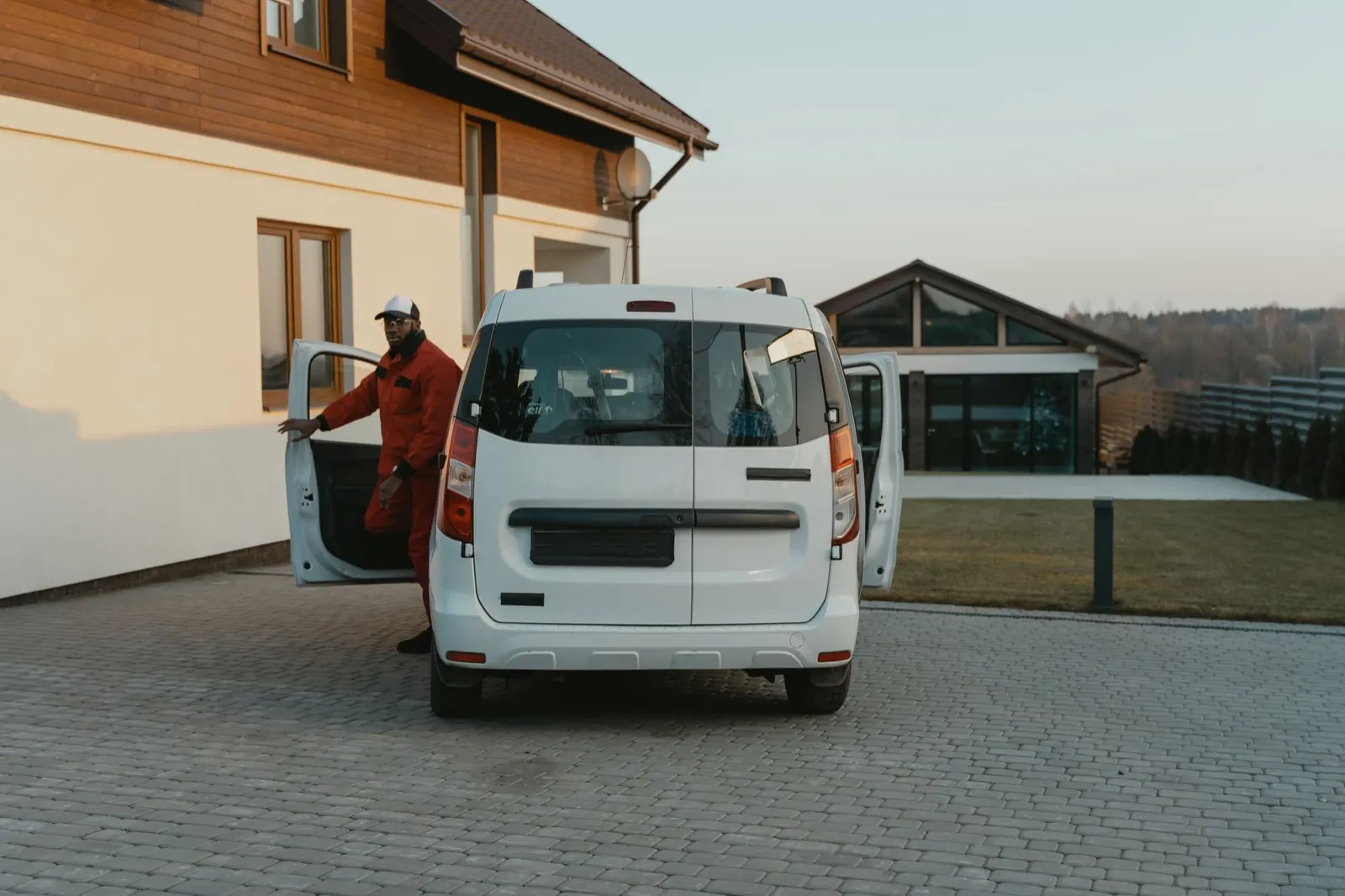 Technician in a red work suit stepping out of a white service van in a driveway